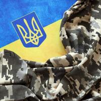 Ukrainian flag and coat of arms with fabric with texture of pixeled camouflage. Cloth with camo pattern in grey, brown and green pixel shapes with Ukrainian trident sign photo