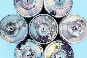 A few used spray cans with blue paint drips lie on texture background of fashion pastel blue color paper photo