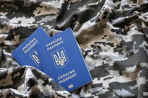 SUMY, UKRAINE - MARCH 20, 2022 Ukrainian foreign passport on fabric with texture of military pixeled camouflage. Cloth with camo pattern in grey, brown and green pixel shapes and Ukrainian ID photo