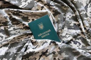 SUMY, UKRAINE - MARCH 20, 2022 Ukrainian military ID on fabric with texture of pixeled camouflage. Cloth with camo pattern in grey, brown and green pixel shapes with Ukrainian army personal token photo