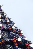 A fragment of a huge Christmas tree with many ornaments, gift boxes and luminous lamps. Photo of a decorated Christmas tree close-up with copy space