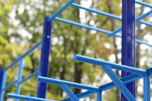 Blue metal pipes and cross-bars against a street sports field for training in athletics. Outdoor athletic gym equipment. Macro photo with selective focus and extremely blurred background