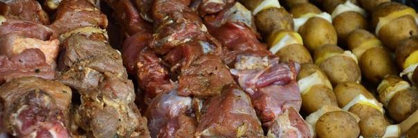 la carne cruda y las patatas se plantan en brochetas de metal. el proceso de cocinar shish kebabs. comida de campamento rusa y ucraniana foto