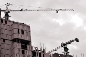 Working tall cranes inside place for with tall buildings under construction against a clear blue sky. Crane and building working progress. Retro tone photo