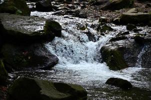 Close-up image of a small wild waterfall in the form of short streams of water between mountain stones photo