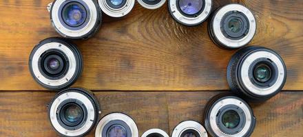 Several photographic lenses lie on a brown wooden background. Space for text photo