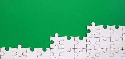 Fragment of a folded white jigsaw puzzle on the background of a green plastic surface. Texture photo with copy space for text