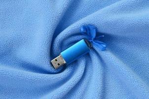 Brilliant blue usb flash memory card with a blue bow lies on a blanket of soft and furry light blue fleece fabric with a lot of relief folds. Memory storage device in women's design photo