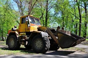 el equipo de mejora de la ciudad quita las hojas caídas en el parque con una excavadora y un camión. trabajo estacional regular en la mejora de los lugares públicos para la recreación foto