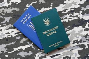 Ukrainian military ID and foreign passport on fabric with texture of pixeled camouflage. Cloth with camo pattern in grey, brown and green shapes with Ukrainian army personal token and passport. photo