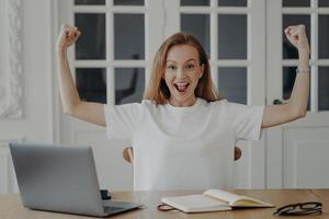 Excited woman gestures power working on project online from home. Concept of win and success. photo