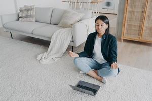 Female practices yoga at laptop on floor, listening meditation to relieve stress after work at home photo