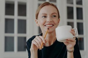 Successful mid adult businesswoman is drinking tea, smiling and dreaming at workplace . photo