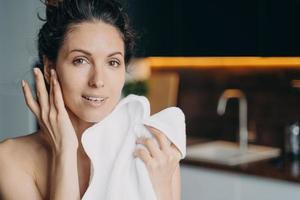 Beautiful woman enjoying healthy smooth skin after washing face, holding towel. Skincare at home photo