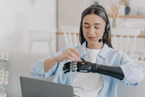 Girl student with disability setting bionic prosthetic arm before work or learning at laptop at home photo