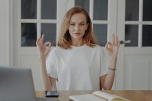 Confident woman gestures ok sitting at the desk in apartment. Successful mid adult businesswoman. photo