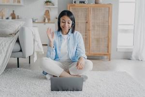 Female coach in headset greeting client while online consultation on laptop by video call at home photo