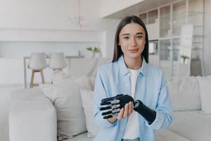 Beautiful caucasian girl with disability taking apart her bionic prosthetic arm, standing at home. photo