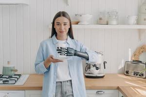 Disabled girl holding cup by bionic prosthetic arm in kitchen. Lifestyle of people with disabilities photo