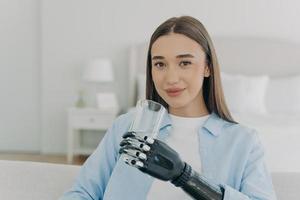 Smiling disabled girl holds glass with water by bionic prosthetic arm. Disability, healthy lifestyle photo