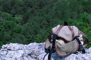 Backpack, tourist backpack lies on a gray rock against the background of green trees. Leisure. photo