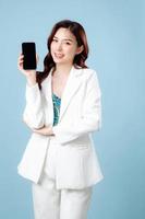 Half body of confident elegant beautiful Asian Business woman wearing white suit smile and holding mobile phone on isolated blue background. Young shopaholic female on copy space. photo