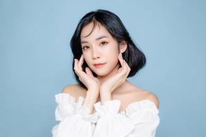 Asian woman short hair with Perfect clean fresh skin. Cute female model with natural makeup and sparkling eyes on blue isolated background. Facial treatment, Cosmetology, beauty Concept. photo