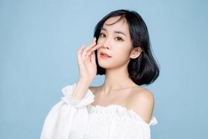 Asian woman short hair with Perfect clean fresh skin. Cute female model with natural makeup and sparkling eyes on blue isolated background. Facial treatment, Cosmetology, beauty Concept. photo