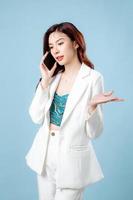 Half body of confident beautiful Asian Business woman wearing white suit talking on mobile phone on isolated blue background. Blank screen smartphone concept photo