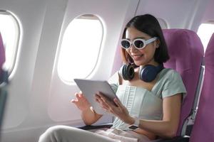 Travel tourism with modern technology and air flights concept, woman sitting in plane with modern digital gadget and searching favourite music playlist in application for listening photo