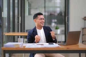 retrato de un empresario asiático de pie con una computadora que muestra felicidad después de una inversión exitosa. foto