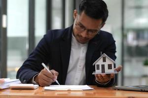Business man hands holding modern house, House model with agent and customer discussing for contract to buy, get insurance or loan mortgage crisis real estate or property. photo