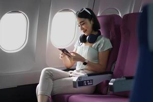 Young woman sitting with phone on the aircraft seat near the window during the flight in the airplane photo