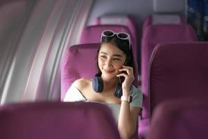 Asian woman sitting on seat in plane cabin near the window and talking on mobile phone. photo