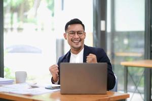 Portrait of an Asian male business owner standing with a computer showing happiness after a successful investment. photo