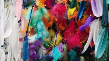 Colorful bird feathers and beads on a ribbon are swinging in the wind in slow motion video