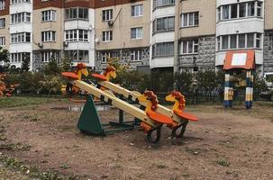 Wooden children's swing, empty playground, horizontal photo. Outdoor leisure for kids, apartment house, bright colorful buildings for children's activity photo