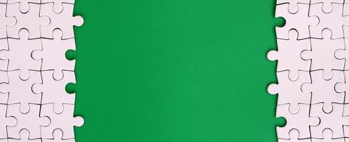 Fragment of a folded white jigsaw puzzle on the background of a green plastic surface. Texture photo with copy space for text