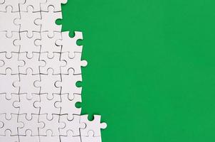 Fragment of a folded white jigsaw puzzle on the background of a green plastic surface. Texture photo with copy space for text