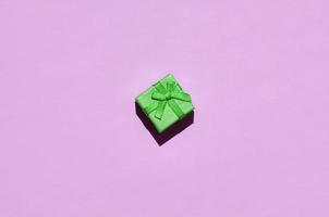 Small green gift box lie on texture background of fashion trendy pastel pink color paper photo