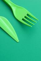 Disposable plastic cutlery green. Plastic fork and knife lie on a green background surface photo