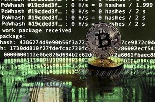 Two bitcoins lies on a videocard surface with background of screen display of cryptocurrency mining by using the GPUs photo