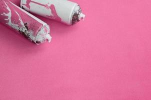 Some used pink aerosol spray cans with paint drips lies on a blanket of soft and furry light pink fleece fabric. Classic female design color. Graffiti hooliganism concept photo