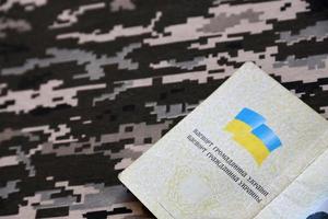 Ukrainian foreign passport on fabric with texture of military pixeled camouflage. Cloth with camo pattern in grey, brown and green pixel shapes and Ukrainian ID photo