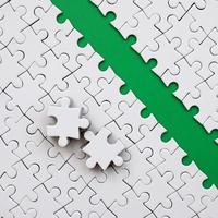 The green path is laid on the platform of a white folded jigsaw puzzle. The missing elements of the puzzle are stacked nearby. Texture image with space for text photo