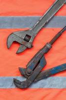 Adjustable and pipe wrenches against the background of an orange signal worker shirt photo