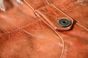 Brown leather texture. Useful as background for any design work. Macro photo of a button on outer clothing made of genuine leather