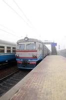 The railway track in a misty morning. The Ukrainian suburban train is at the passenger station. Fisheye photo with increased distortion