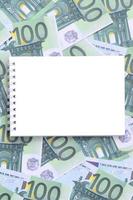 cuaderno blanco con páginas limpias sobre un conjunto de denominaciones monetarias verdes de 100 euros. mucho dinero forma un montón infinito foto
