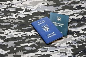 SUMY, UKRAINE - MARCH 20, 2022 Ukrainian military ID and foreign passport on fabric with texture of pixeled camouflage. photo